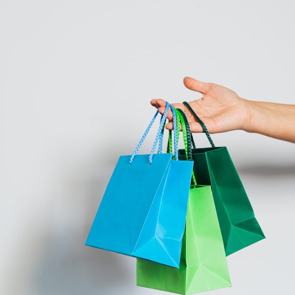 Hand holding three colorful paper shopping bags on a white background.