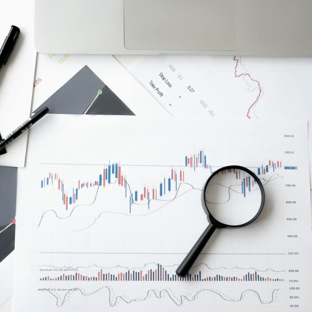 Photo by Anna Nekrashevich Flat lay of stock market analysis documents with magnifying glass, pens, and glasses.