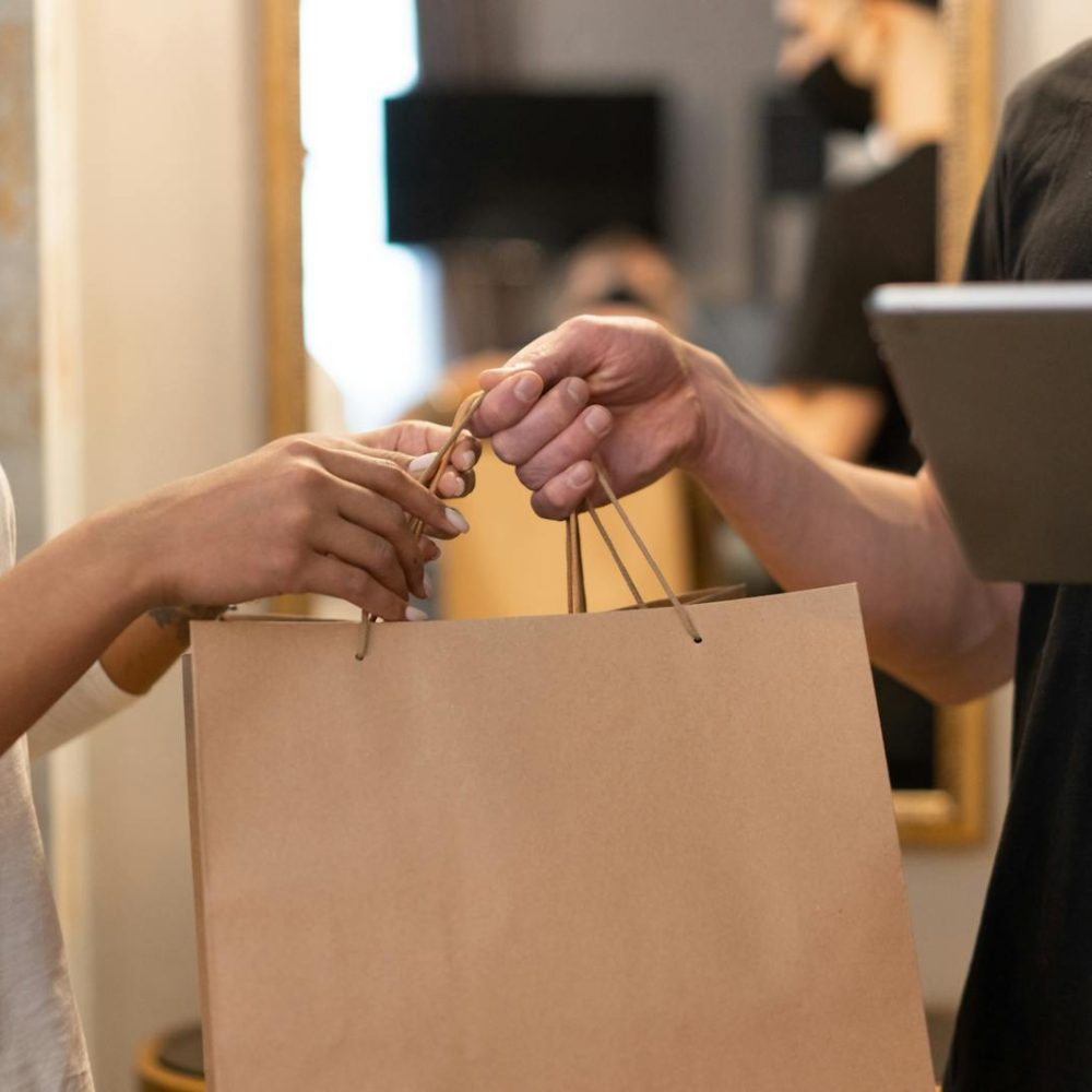 Close-up of hands exchanging a shopping bag indoors, symbolizing modern retail and technology.