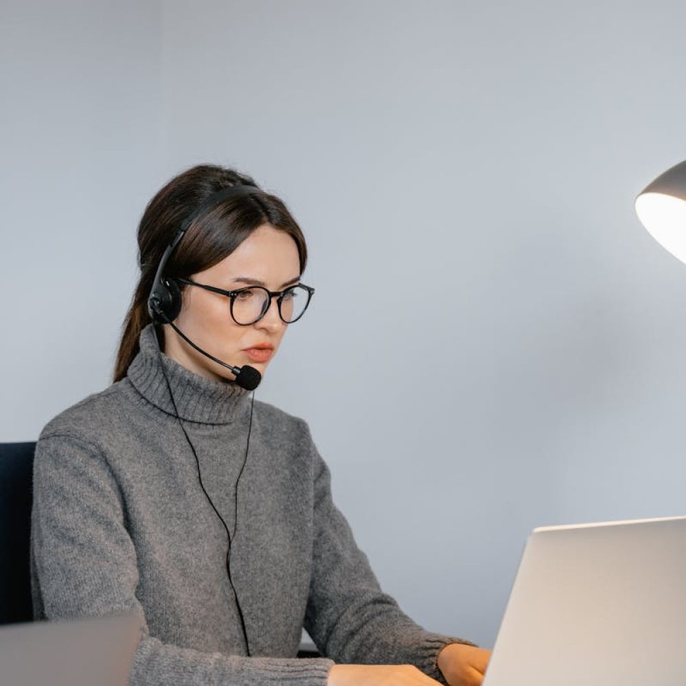 Photo by MART PRODUCTION Focused woman in office with headset, providing customer support on laptop.